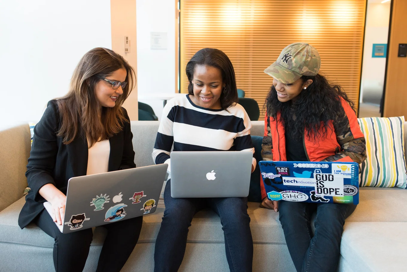 Three people, two laptops, sofa, colorful stickers.